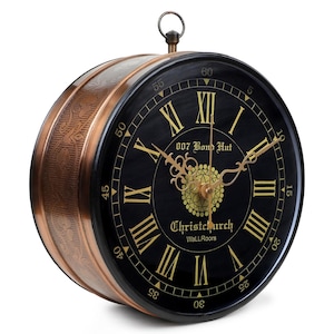 May include: A round wall clock with a black face, gold Roman numerals, and ornate gold hands. The side casing is copper-colored with an embossed floral pattern. The face features the text 007 Bond Hut, Christchurch, and WaLLRoors.