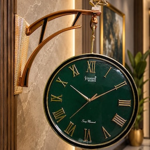 Op de afbeelding: Een dubbelzijdige wandklok met een diepgroene ronde wijzerplaat, gouden Romeinse cijfers en wijzers. De klok hangt aan een decoratieve, bronskleurige metalen beugel met een gouden hertenfiguur. De tekst Sizzero Quartz is zichtbaar op de wijzerplaat.