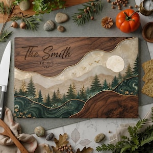 May include: A rectangular wooden serving board featuring a dark walnut wood grain top and bottom section. The center displays a resin landscape with a mountain range, pine trees, a full moon, and birds. The text reads The Smith Est. 2026.