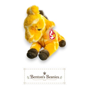 May include: A plush giraffe toy with yellow and orange patterned fur, dark brown hooves, and a dark brown mane. The toy features a red heart-shaped Ty tag attached to its side. Below the toy, the text Benton's Beanies is printed in black.