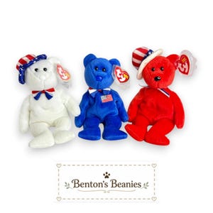 May include: Three plush teddy bears in red, white, and blue. The white bear wears a flag-patterned hat and bow tie. The blue bear has a flag patch on its chest and a striped bow tie. The red bear wears a flag-patterned hat and striped ribbon.