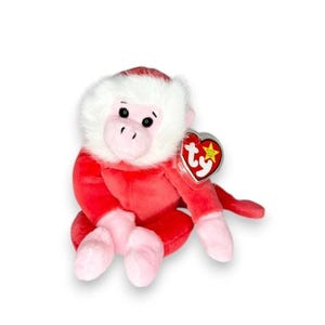 May include: A plush monkey toy with bright red fur on its body and limbs, contrasted by a soft white fur face and light pink hands and feet. The toy features black embroidered eyes and a heart-shaped Ty tag attached to its left arm.