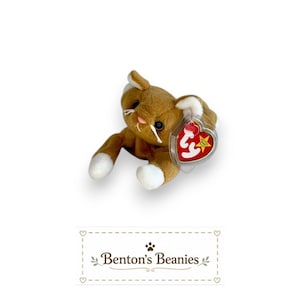 May include: A brown plush cat toy with white paws and inner ears, featuring black eyes, a pink nose, and white whiskers. A heart-shaped red and gold Ty Beanie Baby tag is attached to the ear. Below the toy, the text reads Benton's Beanies.