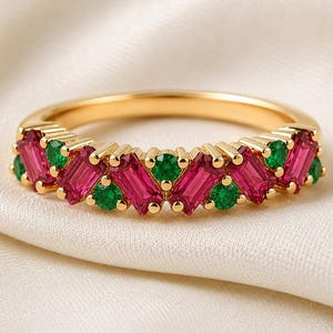 May include: A gold band ring featuring an alternating pattern of rectangular baguette-cut pink stones and round brilliant-cut green stones set in a continuous row across the top half of the metal band, creating a vibrant and colourful jewellery piece.