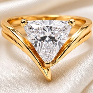 Peut inclure: Une bague en or ornée d'une grande pierre précieuse transparente taille trillion, fixée par un sertissage à trois griffes. L'anneau présente une finition lisse et polie avec un design en V qui soutient la pierre triangulaire.