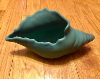 Könnte beinhalten: Ein tealblauer Keramik-Muscheltopf. Der Topf ist wie eine Conchenschale geformt mit einer breiten Öffnung und einem spitzen Ende.