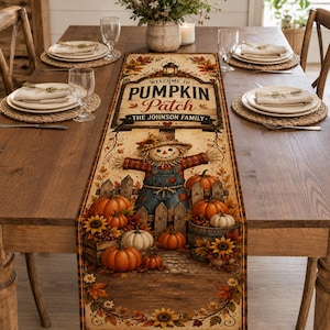 May include: A rectangular table runner featuring a rustic autumn design with a scarecrow, pumpkins, sunflowers, and fall foliage. The text reads Welcome to Pumpkin Patch and The Johnson Family. The runner is displayed on a wooden dining table.