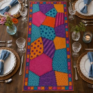 May include: A rectangular table runner featuring a patchwork design of various geometric shapes in vibrant shades of pink, orange, purple, and teal. The fabric displays diverse patterns including polka dots, stripes, and swirls, all bordered by a thin orange frame.