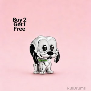 Op de afbeelding: Een zilverkleurige bedel van een cartoonhond met grote ogen, zwarte oren en een groene kraag. De bedel staat tegen een roze achtergrond. De tekst op de afbeelding luidt "Buy 2 Get 1 Free".