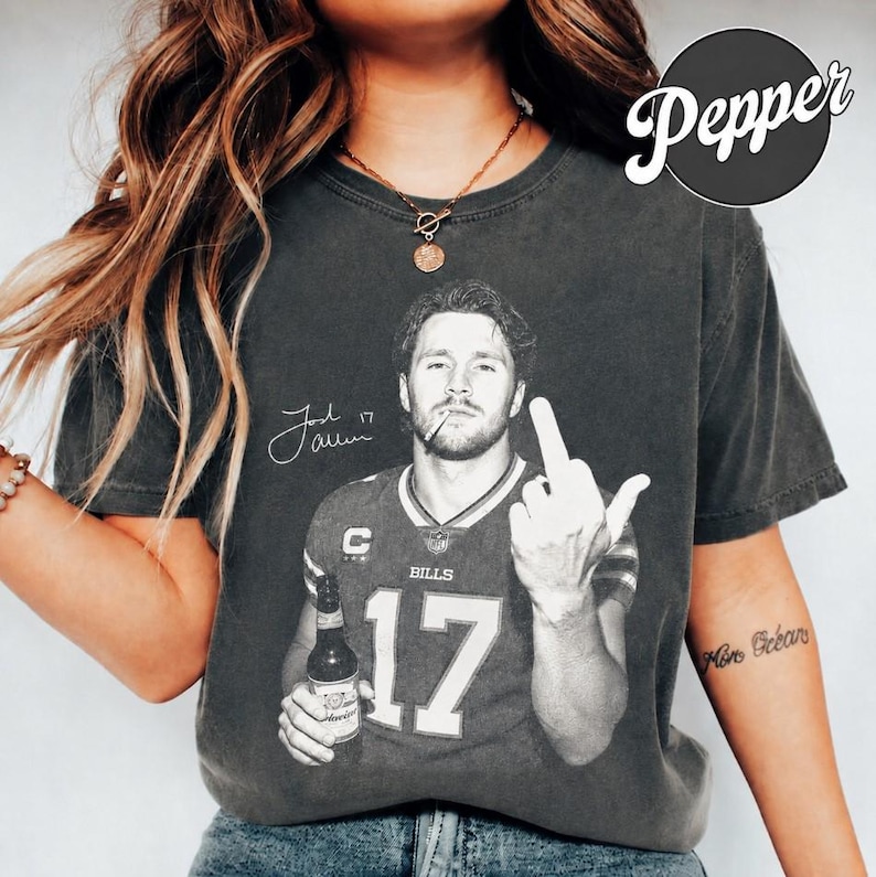 May include: A charcoal gray short-sleeve t-shirt featuring a black and white graphic of a football player in a jersey with the number 17, holding a beer bottle and giving a middle finger gesture. The graphic includes a signature and the text Bills.