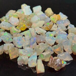 Könnte beinhalten: Eine Ansammlung kleiner, roher Opal-Edelsteine mit unregelmäßiger, gezackter Form. Jeder Stein weist eine durchscheinende, milchig-weiße Grundfarbe mit lebhaften Blitzen aus irisierendem grünem, blauem, orangem und gelbem Licht auf.