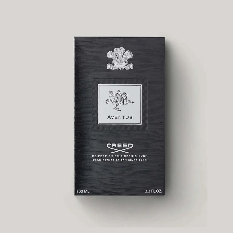 May include: A black rectangular perfume box with a textured surface. It features a silver crest at the top, a central white label with a winged horse illustration and the text AVENTUS, and the CREED logo with the text DE PERE EN FILS DEPUIS 1760.
