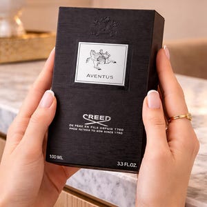 May include: A black rectangular Creed Aventus fragrance box with a textured finish. The front features a silver label with a horse and rider graphic, the text Aventus, Creed, and De Pere En Fils Depuis 1760, 100 ml, and 3.3 fl. oz.