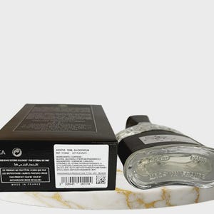 May include: A black rectangular perfume box with white text and a barcode next to a clear glass perfume bottle with a black cap. The box displays the text Aventus 100ml Eau de Parfum, ingredients, and Made in France. The bottle base is visible.