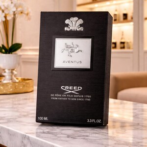 May include: A black rectangular perfume box with a textured finish. It features a silver emblem at the top, a central silver label with the text AVENTUS, and the text CREED DE PERE EN FILS DEPUIS 1760 FROM FATHER TO SON SINCE 1760. It displays 100 ML and 3.3 FL.OZ.