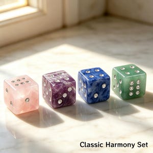 May include: Four gemstone dice in pink, purple, blue, and green. Each die has silver-colored dots and is labeled "Classic Harmony Set". The dice are displayed on a marble surface.