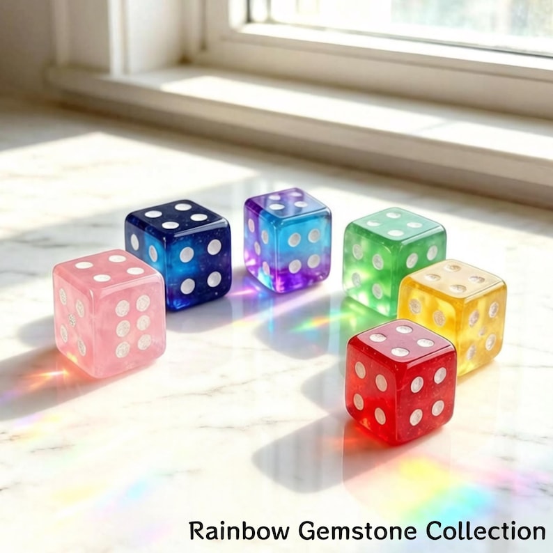 May include: A collection of six colorful gemstone dice. Each die is a different color: pink, blue, purple, green, yellow, and red. The dice have white dots and are arranged on a light-colored surface. Text at the bottom reads "Rainbow Gemstone Collection."