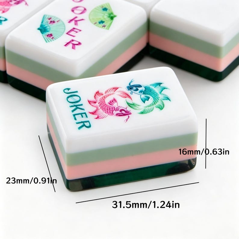 K&ouml;nnte beinhalten: Ein rechteckiger Mahjong-Spielstein mit einer Grafik aus rosa und t&uuml;rkisfarbenen Koi-Fischen und dem Wort JOKER in T&uuml;rkis. Der Stein hat eine wei&szlig;e Oberseite, eine hellgr&uuml;ne Schicht, eine rosa Schicht und eine dunkelgr&uuml;ne Basis. Ma&szlig;e: 31,5 mm x 23 mm x 16 mm.
