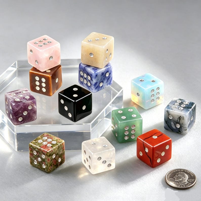 May include: A collection of gemstone dice in various colors, including pink, brown, black, blue, green, red, and white. Each die features white dot markings. The dice are displayed on a clear, geometric stand, with a US quarter for size comparison.