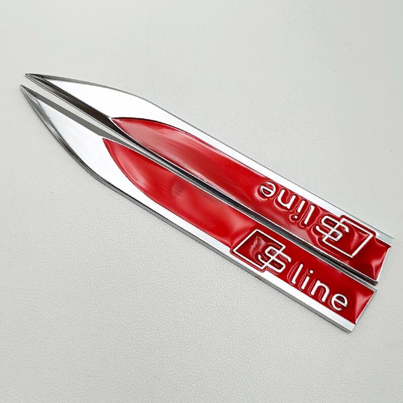 May include: Two silver and red S line car emblems. The emblems are elongated with a pointed end. The red section has the text "S line" in white. The emblems are likely for a car.