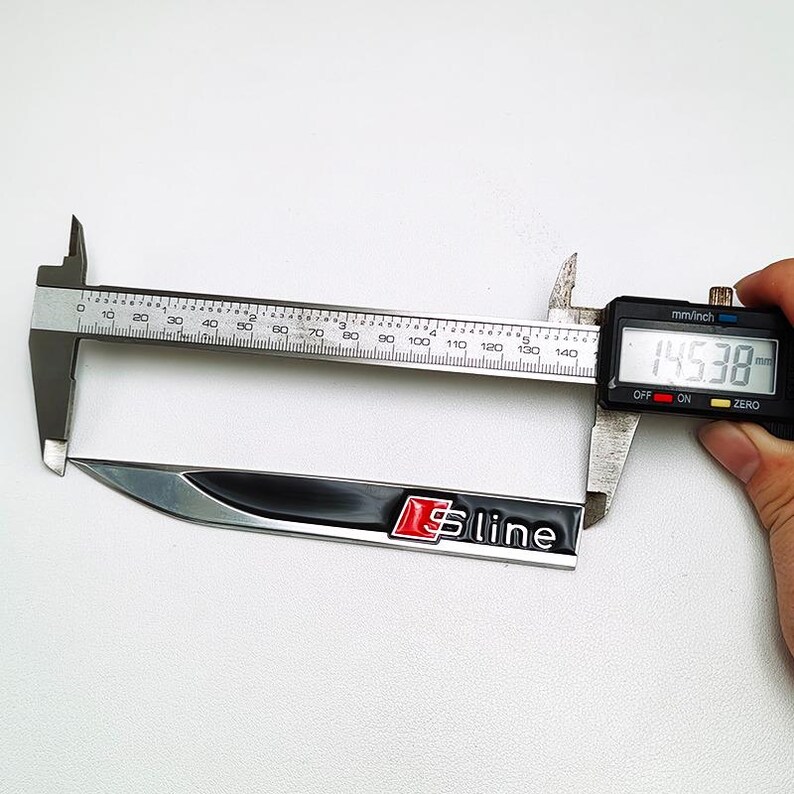 May include: A black and silver S line emblem is measured with a digital caliper. The emblem has a red "S" and the word "line" in white. The caliper reads 145.38 mm.