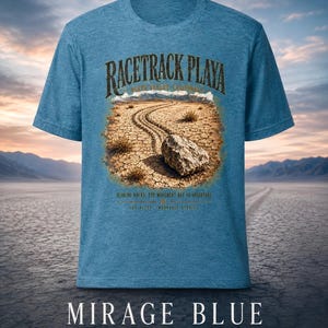 Puede incluir: Una camiseta azul jaspeado con un gr&aacute;fico de Racetrack Playa en el Valle de la Muerte, California. El estampado muestra una roca con un rastro sobre tierra agrietada, con el texto "RACETRACK PLAYA", "SLIDING ROCKS: THE MOVEMENT HAS NO OBSERVERS".