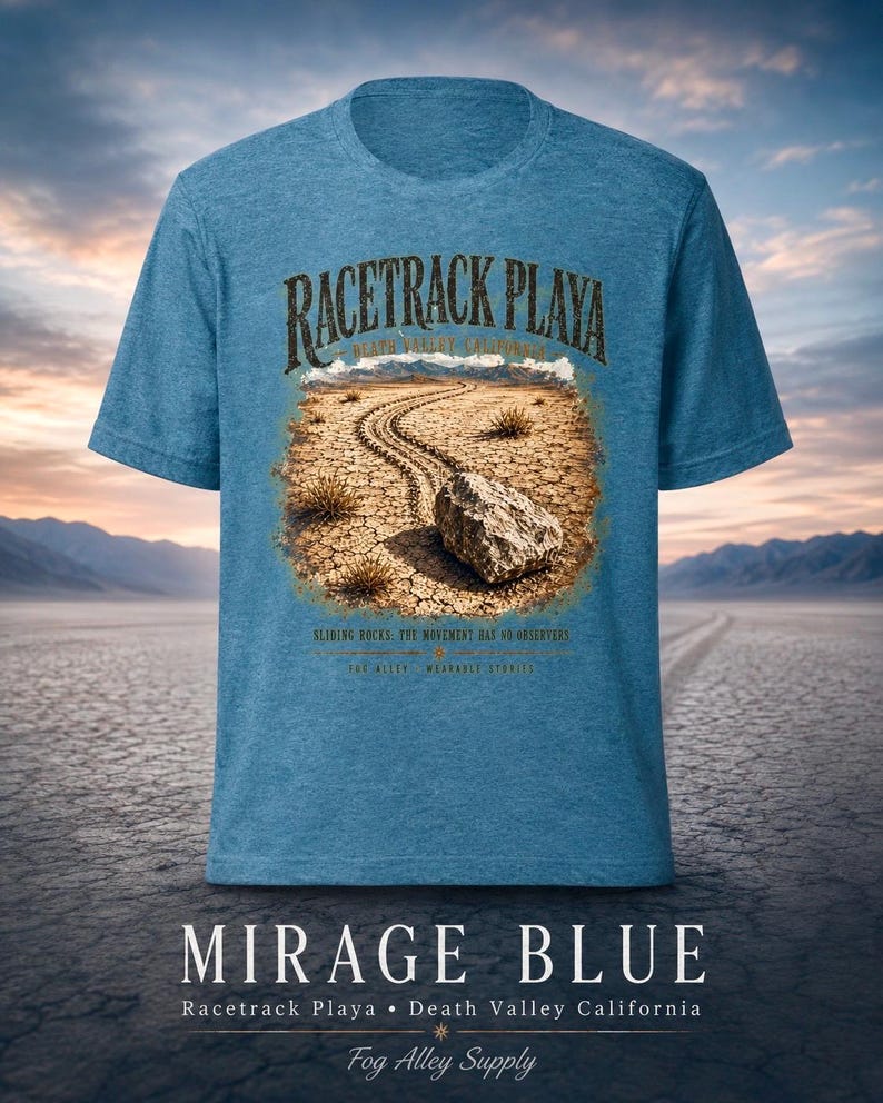 Puede incluir: Una camiseta azul jaspeado con un gr&aacute;fico de Racetrack Playa en el Valle de la Muerte, California. El estampado muestra una roca con un rastro sobre tierra agrietada, con el texto "RACETRACK PLAYA", "SLIDING ROCKS: THE MOVEMENT HAS NO OBSERVERS".