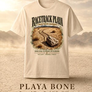 Puede incluir: Una camiseta de color crema con un gr&aacute;fico de Racetrack Playa en el Valle de la Muerte, California. El dise&ntilde;o muestra una roca sobre tierra agrietada con el texto "RACETRACK PLAYA", "SLIDING ROCKS: THE MOVEMENT HAS NO OBSERVERS" y "FOG ALLEY WEARABLE STORIES".