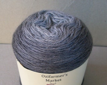 May include: A skein of yarn in a gradient of grey and blue colours. The yarn is wrapped around a cardboard tube with a label that reads "Ozifarmer's Market" and "Rapture".