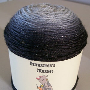 Könnte beinhalten: Eine Garnrolle mit Ombre-Farbverlauf in Schwarz und Silber mit Glitzer. Das Garn ist mit "Ozfarmer's Market" und "Glitterata" beschriftet.