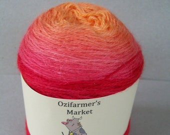 May include: A vibrant ball of yarn, transitioning from orange to red hues. The yarn is wrapped with a white label featuring "Ozifarmer's Market" text and a cartoon cow knitting. The word "Rapture" is printed below the cow.