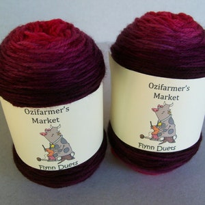 May include: Two skeins of yarn in a gradient of pink to dark purple. The yarn is labeled "Ozifarmer's Market" and "Flynn Duets".