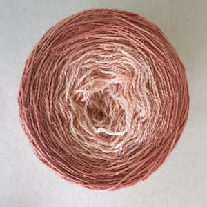 May include: A ball of yarn in a gradient of colours, shifting from a dark reddish-brown to a pale peach. The yarn is tightly wound, displaying the texture of the fibres. Suitable for knitting or crochet projects.