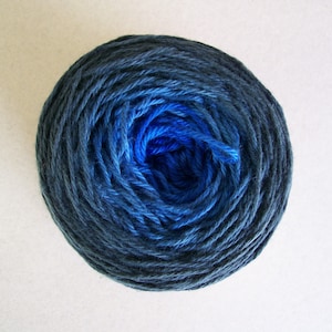 May include: A ball of yarn with a gradient of blue and black colors. The yarn is wound into a tight ball, with the blue color at the center and the black color at the edges.