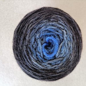 May include: A ball of yarn with a gradient of colors, transitioning from dark navy blue to lighter shades of blue in the center. The yarn is tightly wound, creating a circular shape. The yarn is likely made of wool or a similar fiber.