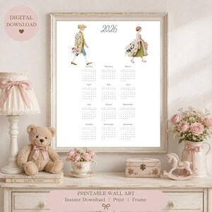 Könnte beinhalten: Ein Wandkalender für 2026 mit zwei illustrierten Figuren in historischer Kleidung, eine mit einem Blumenmantel und die andere in einem grünen Kleid mit Blumenakzenten. Der Kalender zeigt alle zwölf Monate mit dem Text 2026 oben.