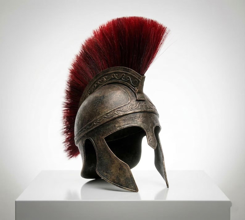 May include: A bronze-colored metal helmet with a weathered, aged finish and an intricate embossed scroll pattern along the brow. The helmet features a prominent, tall crest made of stiff, deep red bristles that arch over the top.