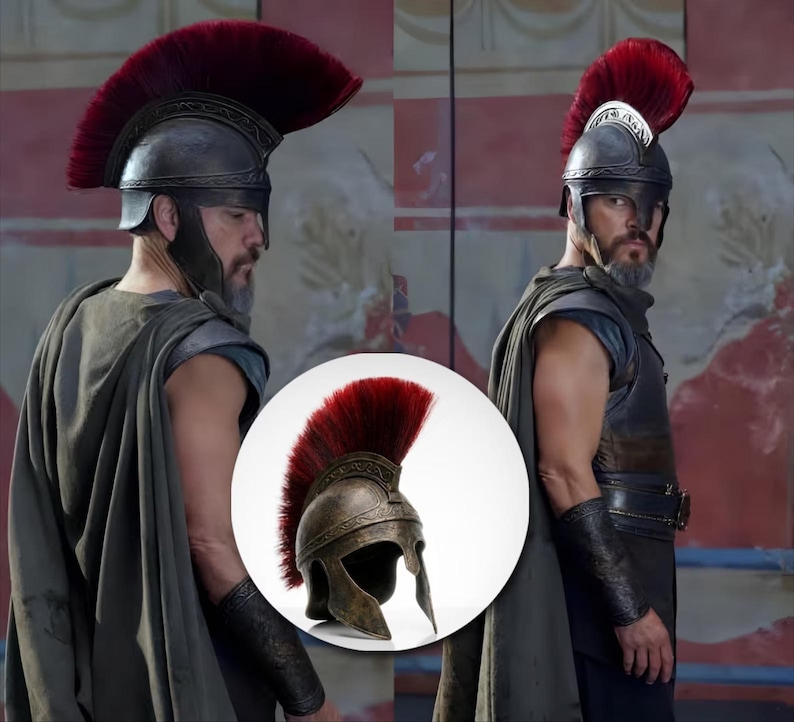 May include: A metallic bronze-toned helmet featuring an ornate embossed band along the crest and a prominent, tall, deep red brush plume extending from the front to the back, designed with a wide face opening and protective cheek guards.