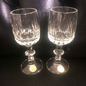 Puede incluir: Dos copas de vino de cristal transparente con cortes verticales texturizados en el cuenco y un tallo facetado. Las copas tienen una base redonda con una peque&ntilde;a pegatina. Las copas est&aacute;n sobre una superficie oscura.