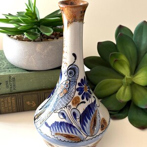 May include: A ceramic vase with a white base, decorated with blue and brown floral and bird patterns. The vase has a narrow neck and a flared base. The rim is dark brown. The vase is approximately 20 cm tall.
