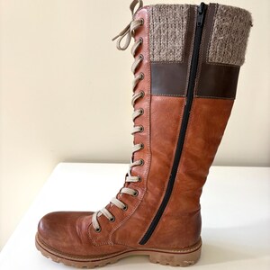 May include: A brown leather boot with a knitted cuff and a side zip. The boot has a lace-up front and a sturdy sole. The leather has a worn look, and the boot is designed for cold weather, suitable for various outdoor activities.