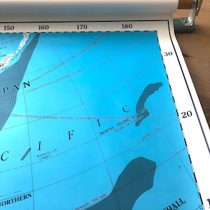 May include: A detailed map of the Pacific Ocean, featuring the North Tropic and the Marshall Islands. The map is rolled up with a wooden and metal holder. The map shows distances in kilometers and miles.