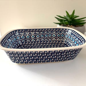 May include: A rectangular ceramic baking dish featuring a deep blue and white pattern with small light blue accents. The interior and exterior walls are decorated with a repeating geometric motif, while the rim is smooth and off-white in colour.