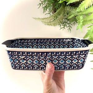 May include: A rectangular ceramic baking dish featuring a repeating geometric pattern in shades of dark blue, light blue, and white. The dish has integrated handles on the sides and a smooth, glazed finish with a decorative border design.