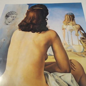 May include: A print of a surrealist painting featuring a nude figure with brown hair, seated and facing away. The background includes a classical bust, a desert landscape, and architectural elements, all rendered in a dreamlike style with a blue sky.