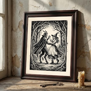 May include: A framed black and white woodcut-style print depicting a horned, caped figure dancing with a person wearing a witch hat and dress in a forest setting. The artwork is enclosed in a dark brown wooden frame with a simple, clean border.