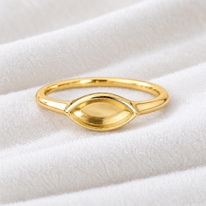 May include: A polished gold ring featuring a central marquise-shaped element with a smooth, concave surface. The band is slender and rounded, maintaining a consistent metallic finish throughout the entire piece of jewelry.