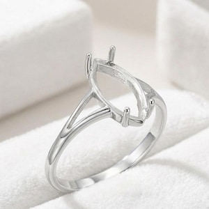 May include: A silver-toned metal ring setting featuring a marquise-shaped basket with four prongs designed to hold a gemstone. The band has a split shank design that tapers as it connects to the central setting, creating a clean and polished look.