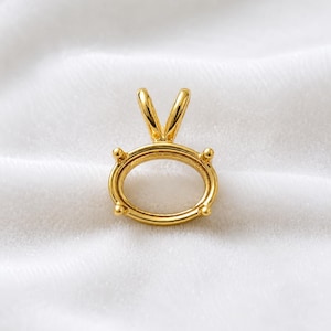 May include: A polished gold-tone oval pendant setting featuring a four-prong mounting design. The pendant includes a V-shaped bail at the top, designed to hold a gemstone securely within its smooth, rounded metal frame and prong structure.