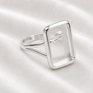 May include: A polished silver ring featuring a large, empty rectangular bezel setting. The band is split into two thin arms that connect to the sides of the rectangle. The inner surface of the band is clearly stamped with the hallmark 925.